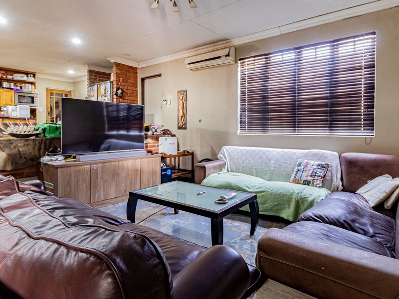 Open plan living area featuring a brick fireplace, air conditioning, and integrated kitchen space with recessed lighting and venetian blinds.