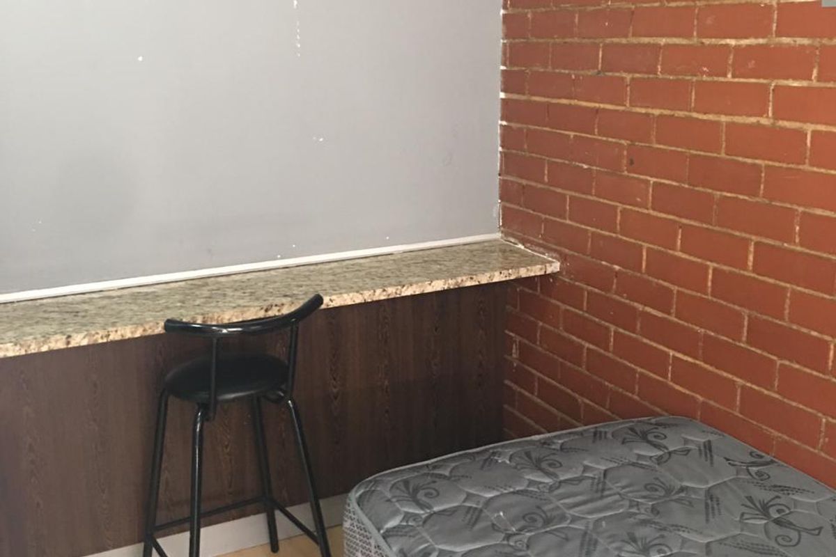 A bedroom featuring an exposed brick wall, laminate flooring, and a built-in granite countertop desk area.
