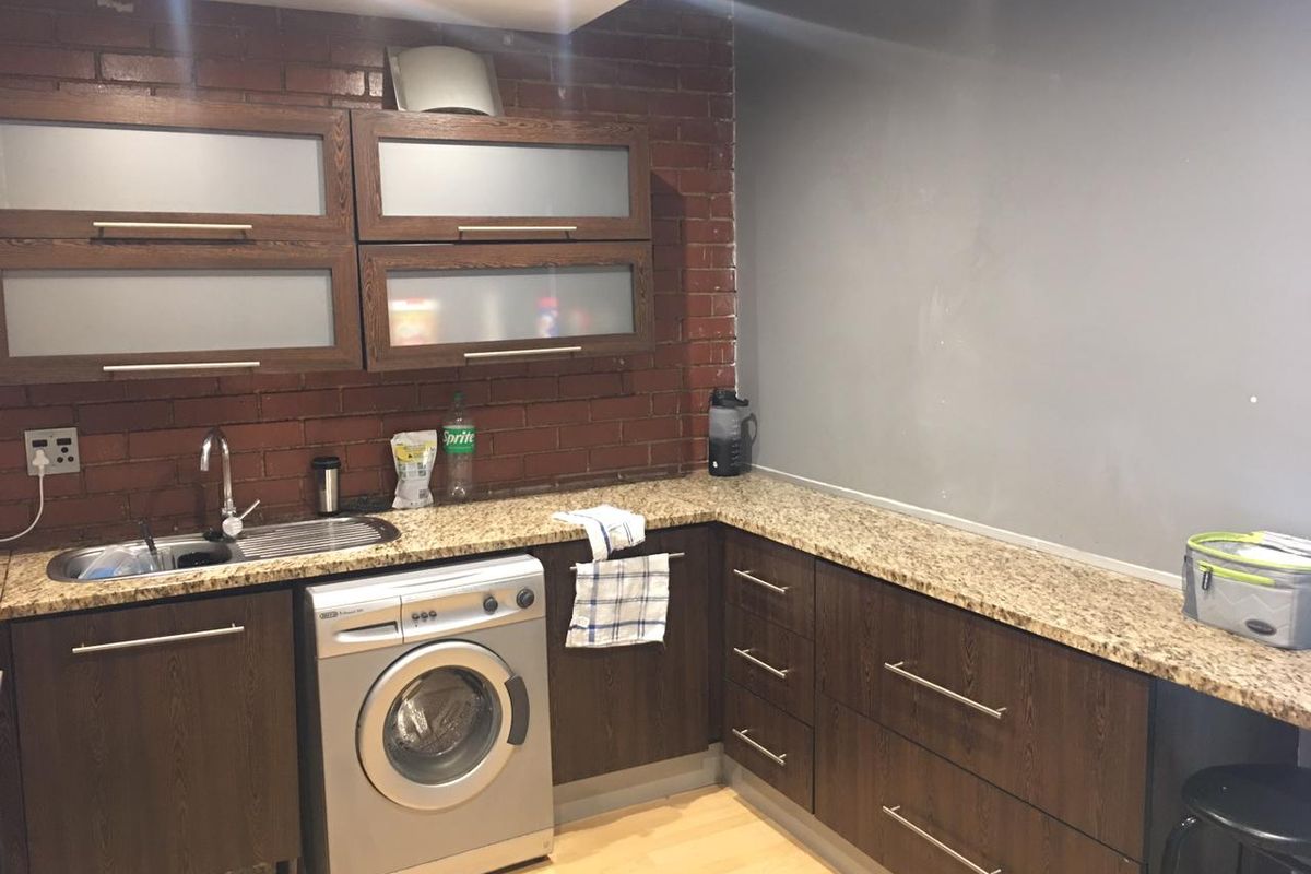 A functional kitchen featuring dark wood cabinetry, granite countertops, an exposed brick backsplash, and integrated laundry plumbing.