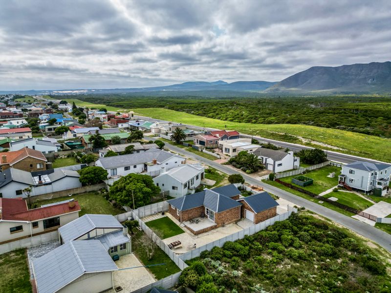 An aerial view of a residential neighborhood featuring a single-story brick house with a pitched roof, paved driveway, and surrounding garden area.