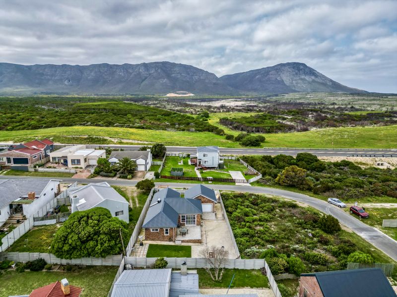 Aerial view of a residential property featuring a metal roof, paved patio, and driveway, set against a scenic mountain and coastal landscape.