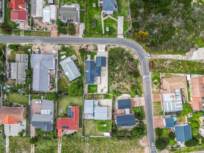 An aerial view of a residential neighborhood showing multiple houses, driveways, landscaped lawns, and roof-mounted solar panels.