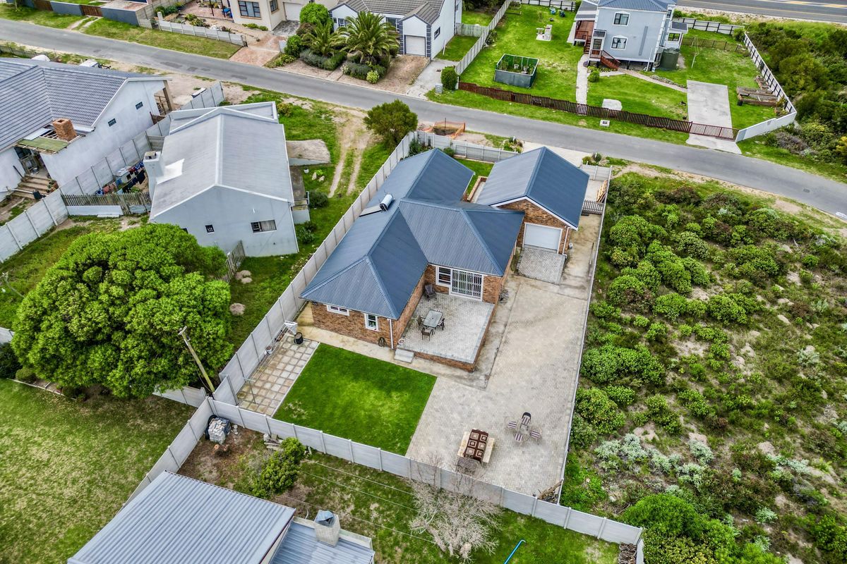 Aerial view of a residential property featuring a metal roof, brick exterior, paved driveway, and a private fenced backyard with a patio area.