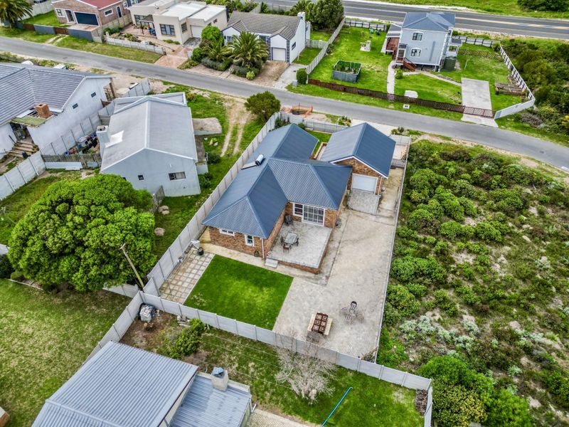 Aerial view of a residential property featuring a metal roof, brick exterior, paved driveway, and a private fenced backyard with a patio area.