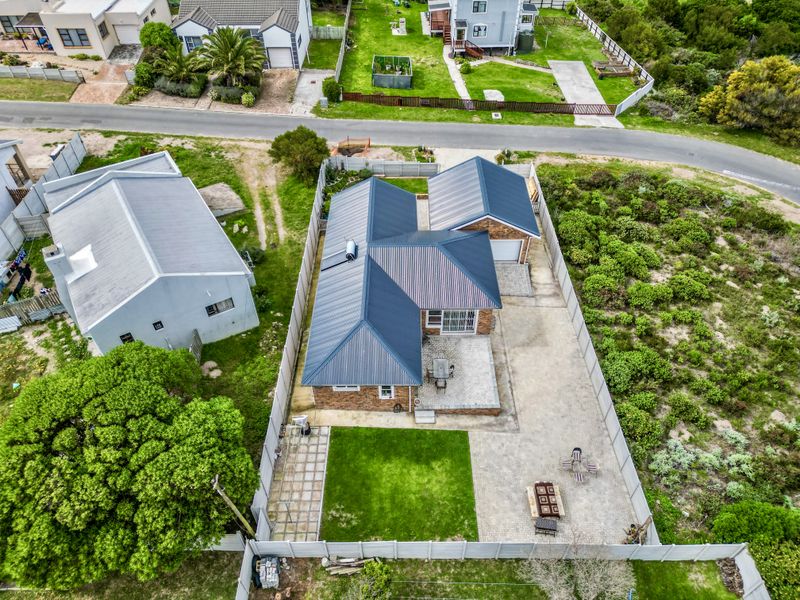 Aerial view of a residential property featuring a metal roof, paved patio area, private garden, and secure perimeter fencing.