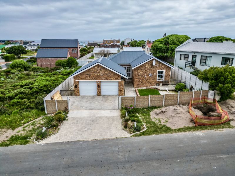 Aerial view of a brick-faced house featuring a double garage, paved driveway, and enclosed yard with ongoing exterior ground works.