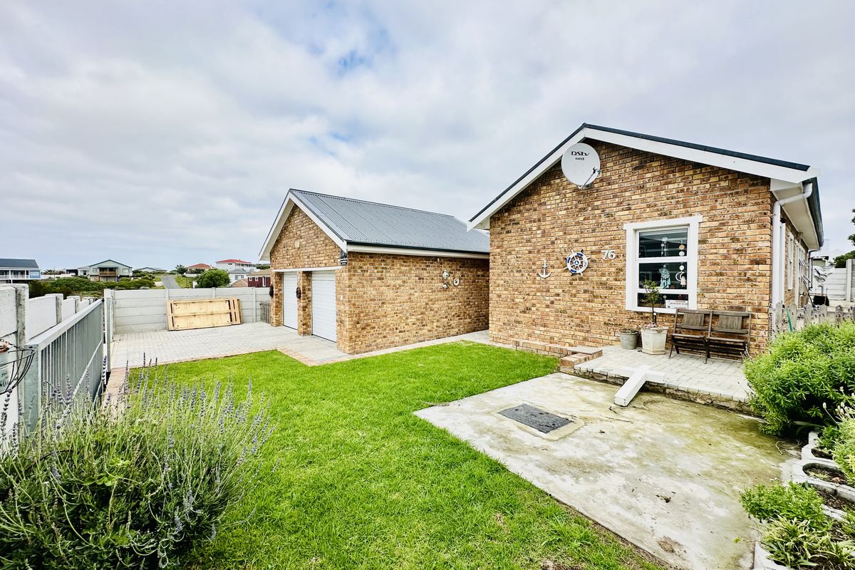 Rear view of the property featuring a face brick facade, double garage, paved driveway, and a concrete patio area set within a private garden.