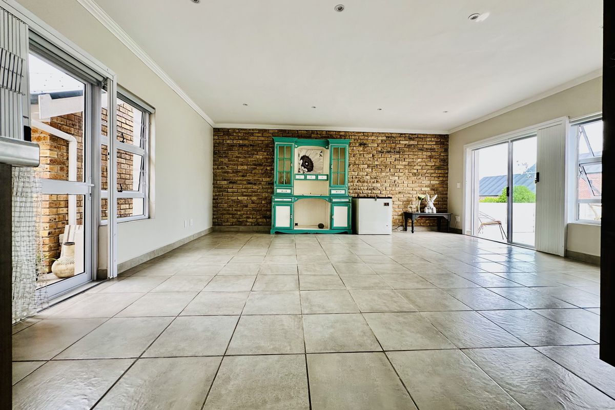 Spacious living area featuring tiled flooring, an exposed brick feature wall, and large sliding glass doors providing ample natural light and outdoor access.