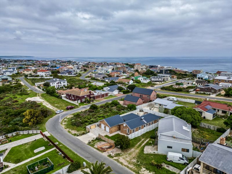 An aerial view of a coastal residential neighborhood featuring various detached houses, paved streets, and proximity to the ocean.