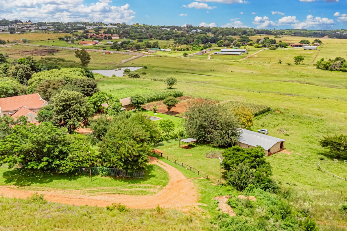 Aerial view of a small holding property featuring a main residence, outbuildings, mature landscaping, and expansive open pasture land.