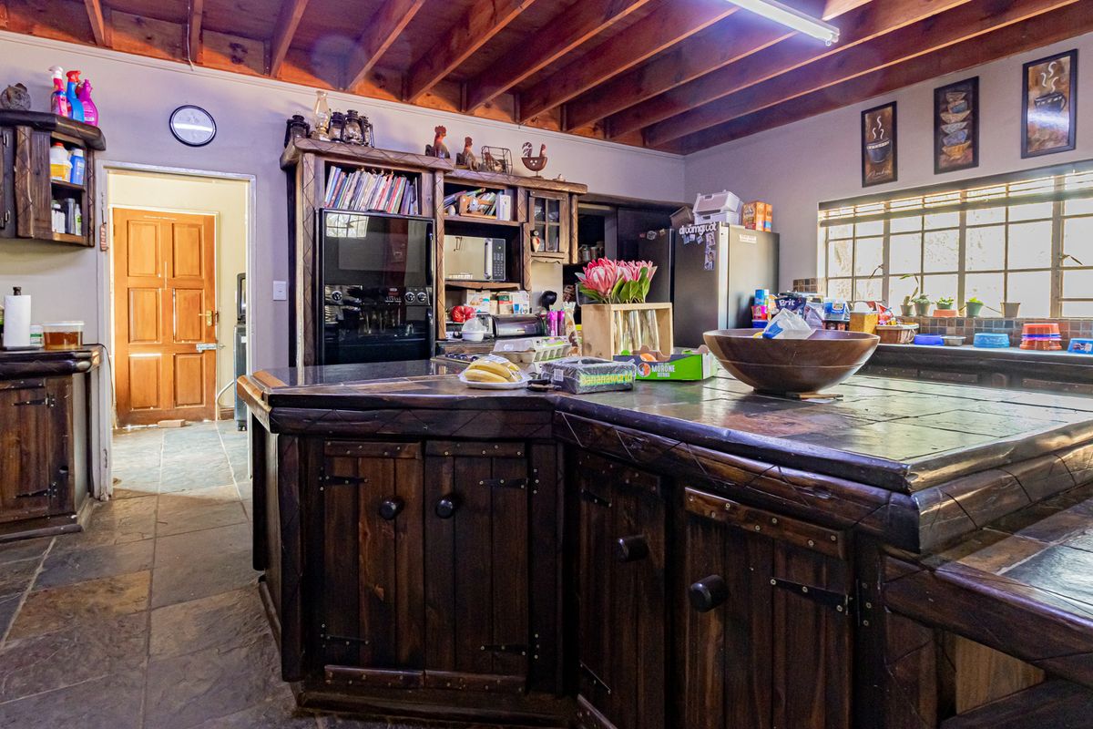Rustic kitchen featuring custom dark wood cabinetry, a large tiled island, slate flooring, and exposed timber ceiling beams, offering a warm, traditional aesthetic.