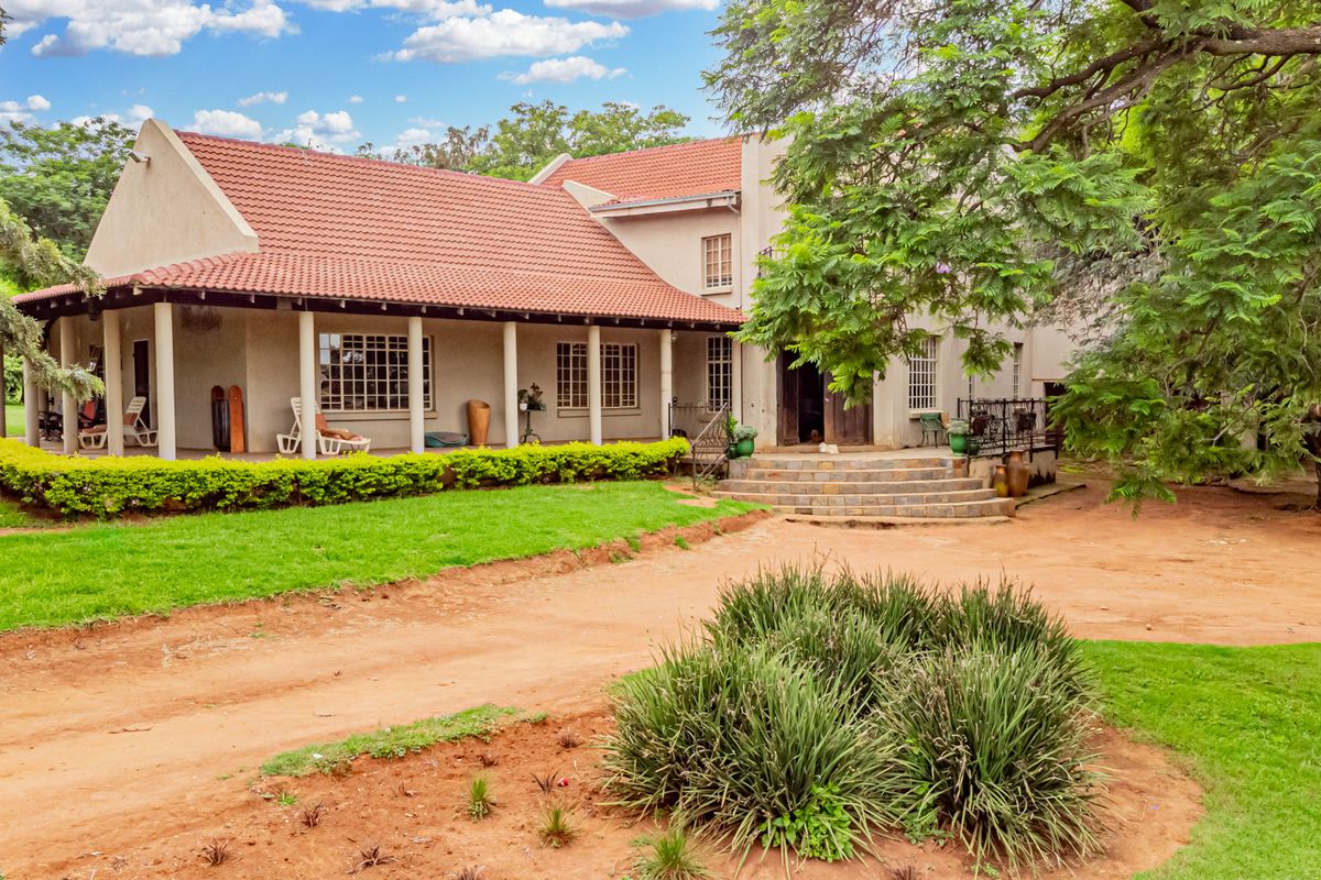 A spacious rear exterior view of the small holding featuring a large covered patio, tiled roof, and stone entrance steps set within a landscaped garden.