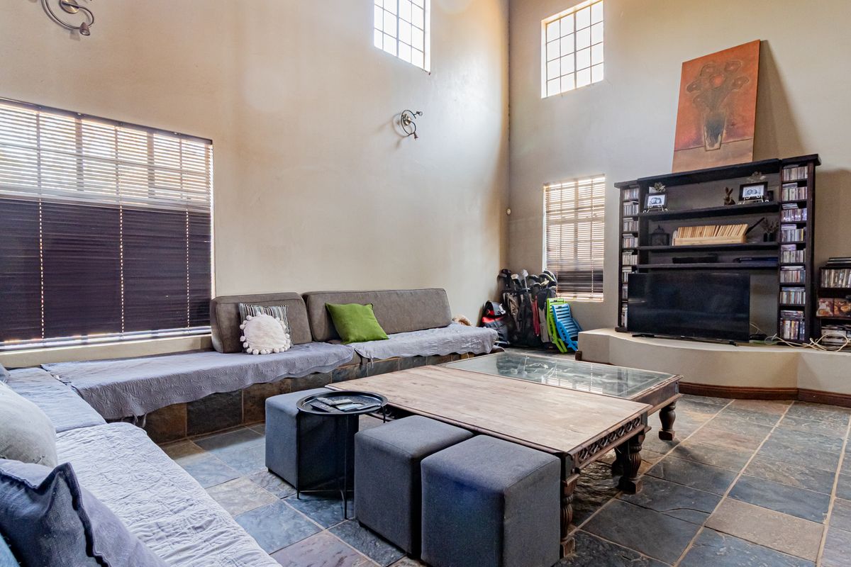 Spacious living room featuring double volume ceilings, slate tile flooring, and a large built-in shelving unit with integrated seating.
