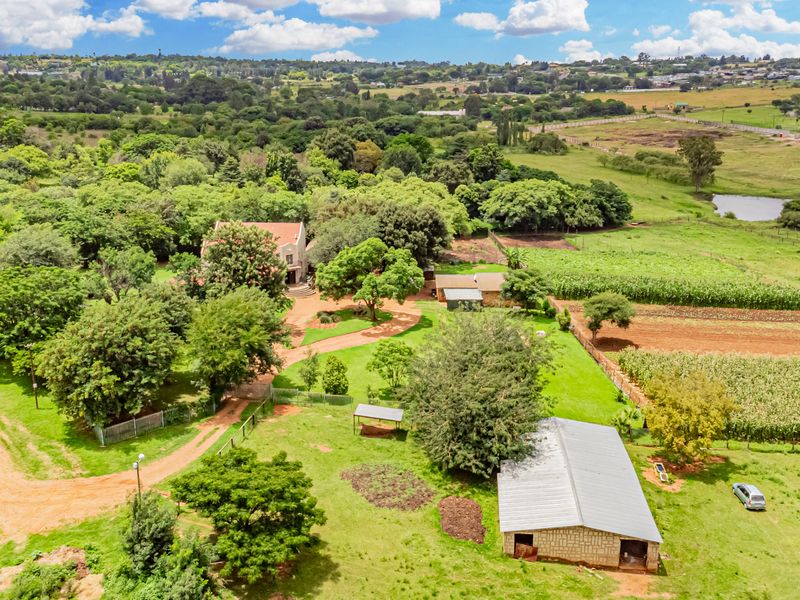 Aerial view of a small holding property featuring a main residence, outbuildings, expansive garden areas, and cultivated agricultural land.
