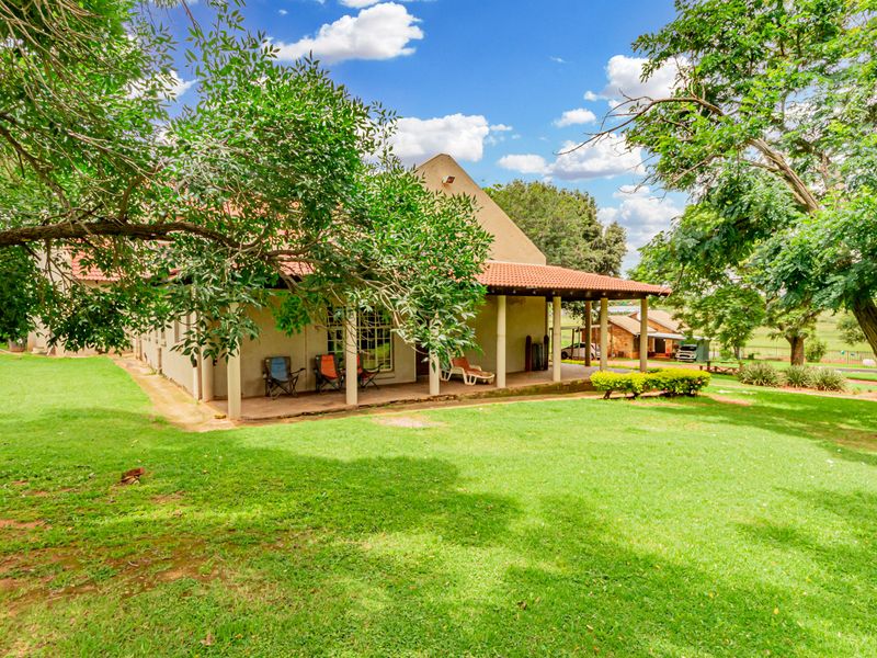 A spacious rear view of the property featuring a covered patio area overlooking a well-maintained, expansive green garden with mature trees.