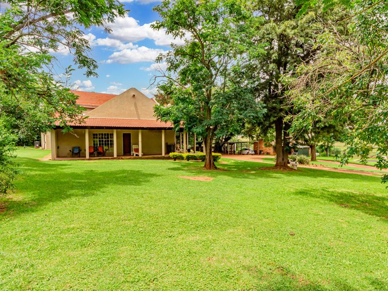 A view of the rear elevation of the small holding, featuring a covered patio, terracotta roof tiles, and expansive mature garden space.