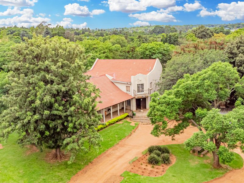 Aerial view of a large small holding property featuring a traditional home with a terracotta tile roof, covered veranda, and expansive surrounding gardens.