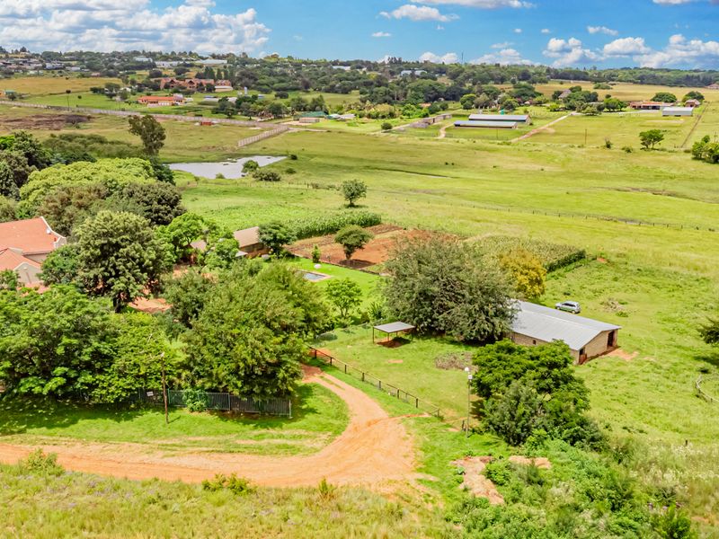 Aerial view of a small holding property featuring a main residence, outbuildings, mature landscaping, and expansive open pasture land.