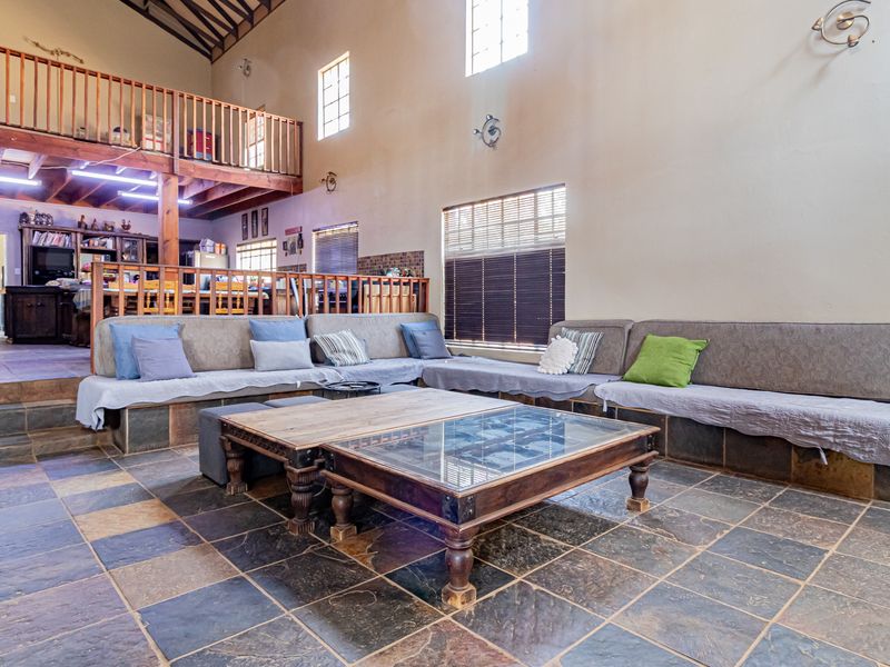 Spacious open-plan living area featuring slate tile flooring, exposed roof trusses, and a mezzanine level with a wooden balustrade and staircase.