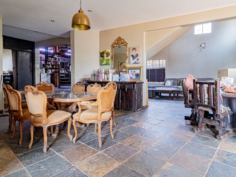 Spacious open-plan living and dining area featuring natural slate tile flooring, a unique spiral staircase, and integrated shelving, offering a versatile layout.
