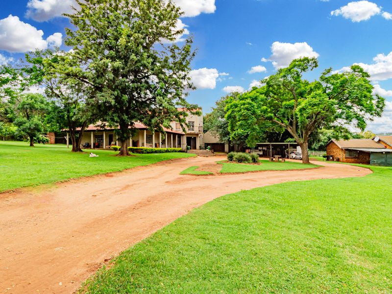 Spacious small holding property featuring a main residence with a covered patio, expansive green lawns, mature trees, and a secondary outbuilding.