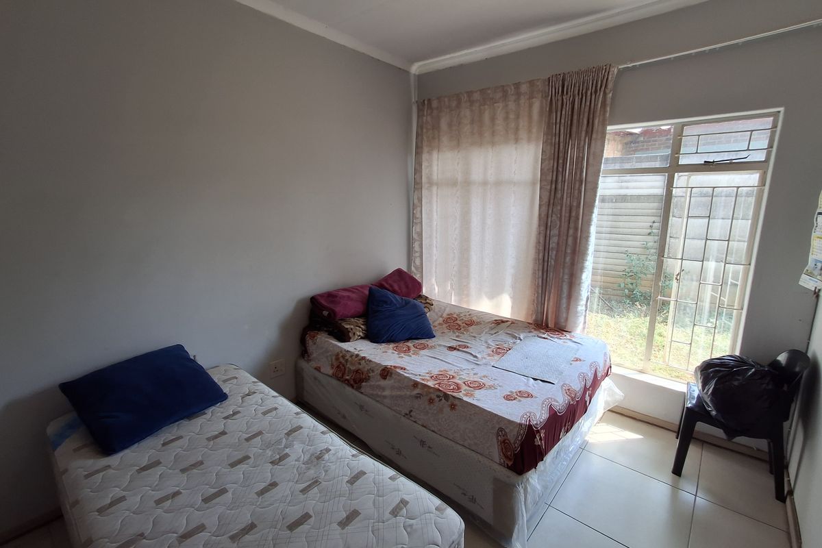 A functional bedroom featuring tiled flooring and a large window with security bars, providing natural light and access to the exterior.