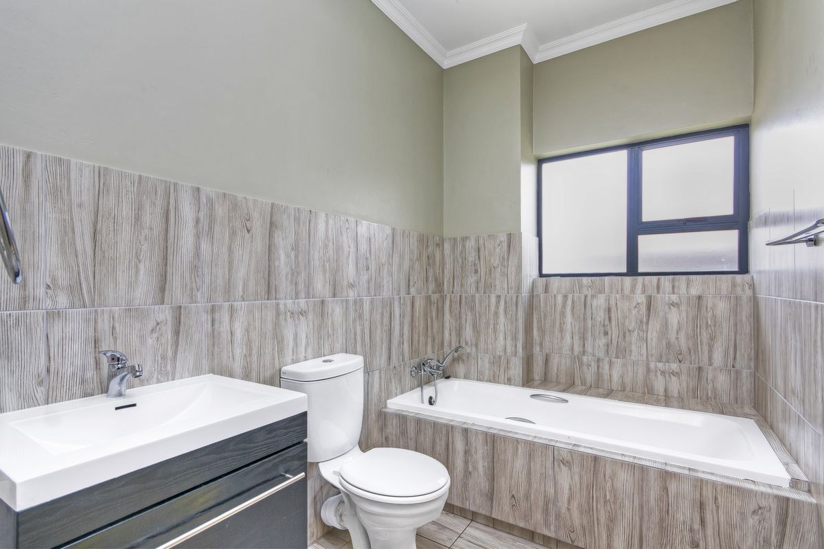 Modern bathroom featuring wood-look tiled walls, a built-in bathtub, a contemporary vanity with basin, and a toilet.
