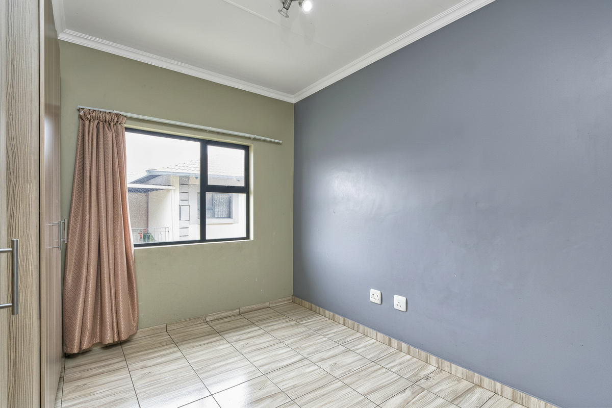 A bright, empty bedroom featuring tiled flooring, built-in wooden cupboards, and a large window providing natural light.