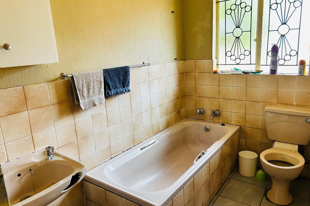A dated bathroom featuring a bathtub, pedestal basin, and toilet with tiled walls and a security window grille.