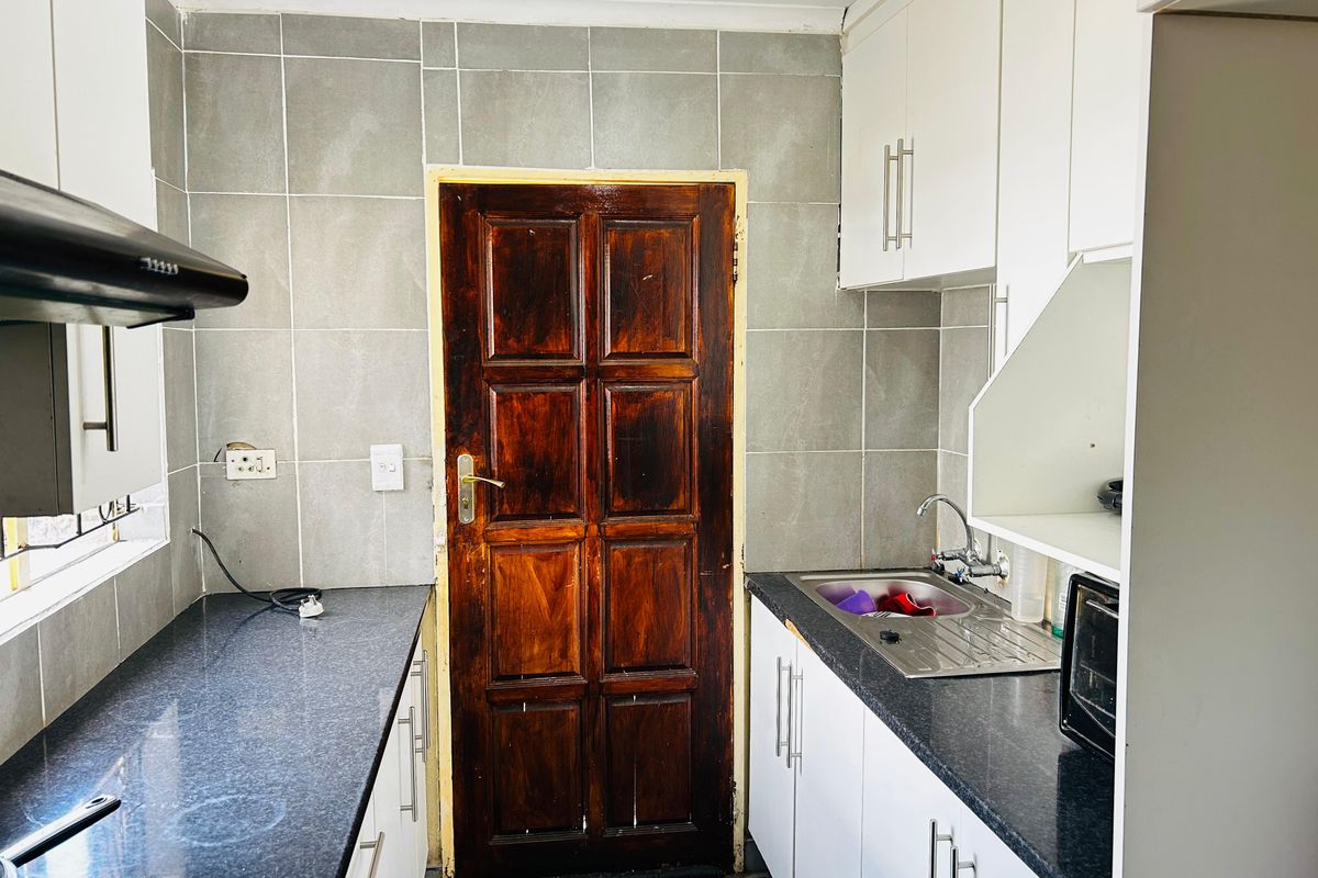 Compact kitchen featuring granite countertops, white cabinetry, tiled backsplash, and a stainless steel sink with an integrated extractor fan.