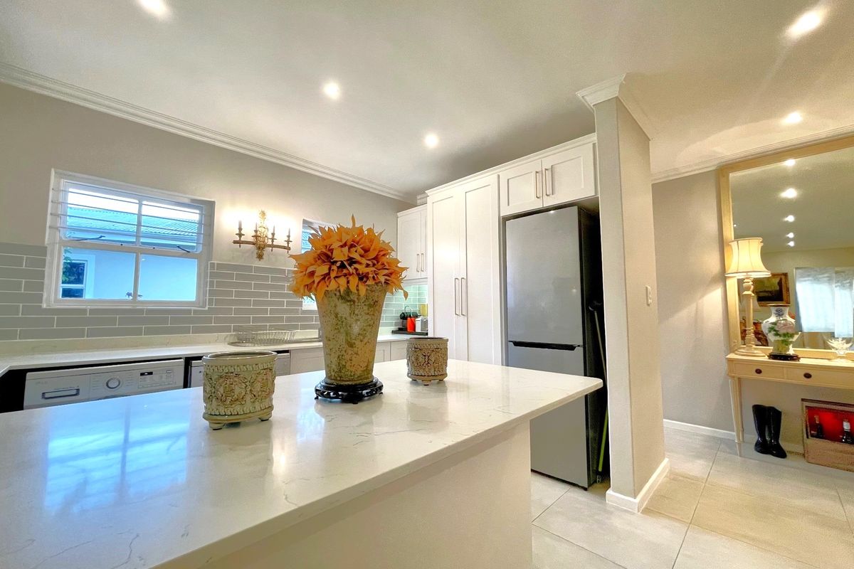 Modern kitchen featuring a central island with stone countertops, subway tile backsplash, and integrated cabinetry, flowing into an adjacent hallway area.