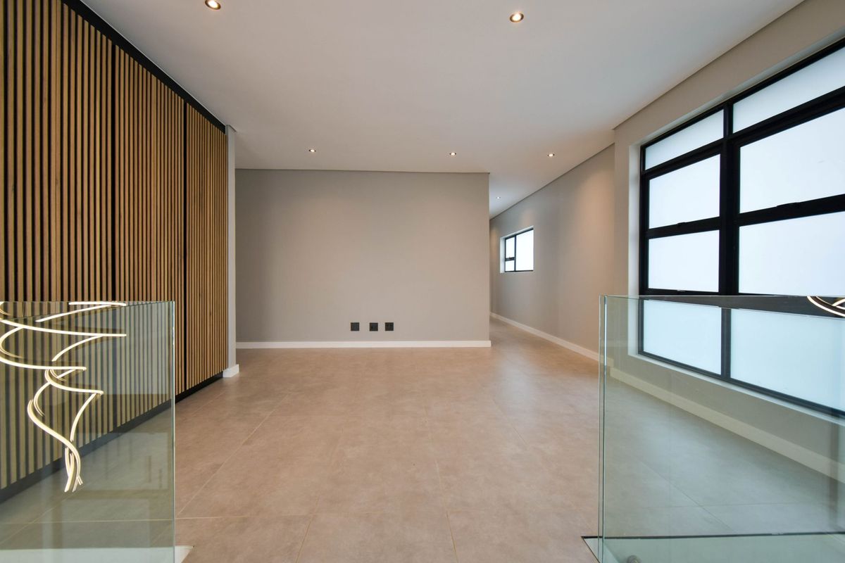 A modern, open-plan living area featuring sleek tiled flooring, recessed downlighting, a decorative timber slat feature wall, and a contemporary glass balustrade.