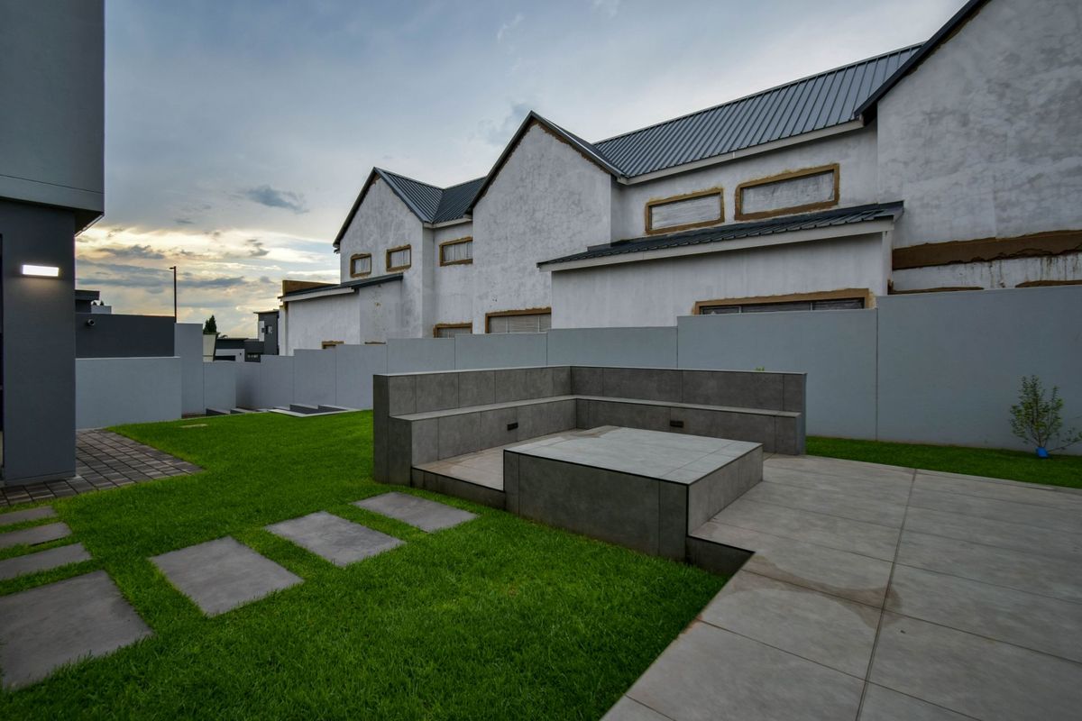 A modern rear garden area featuring a built-in tiled seating bench and fire pit, set against a property currently undergoing exterior finishing works.