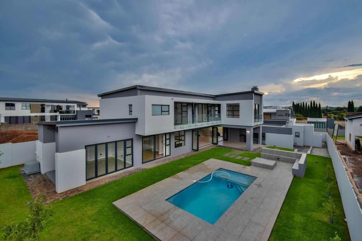 Aerial view of a modern two-story residence featuring a swimming pool, paved patio area, and landscaped garden.