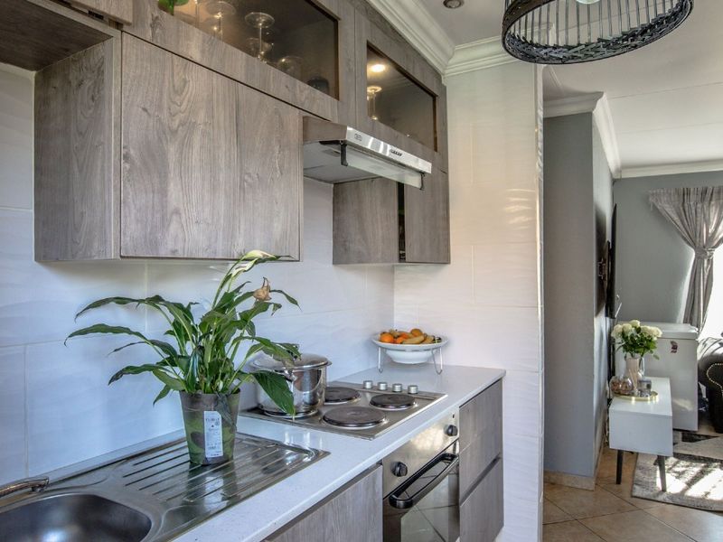 Modern kitchen featuring wood-grain cabinetry, integrated electric hob, oven, extractor fan, and a stainless steel sink with a clean tiled backsplash.