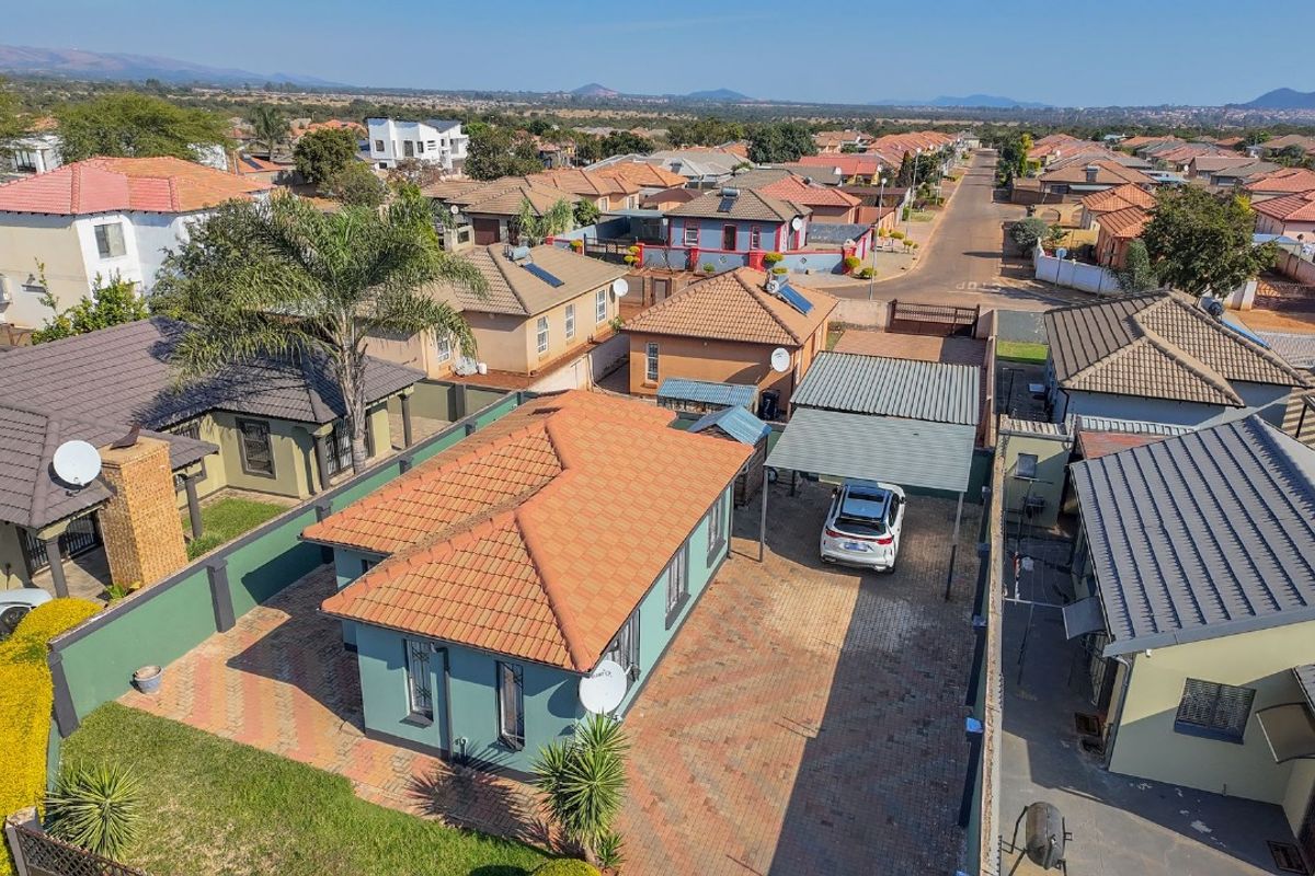 Aerial view of a residential property featuring a tiled roof, paved driveway, and a carport within a suburban neighborhood setting.