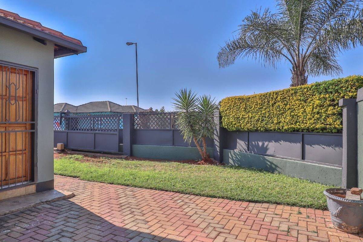 A private rear garden area featuring brick paving, a well-maintained lawn, and secure boundary walling with integrated hedging.