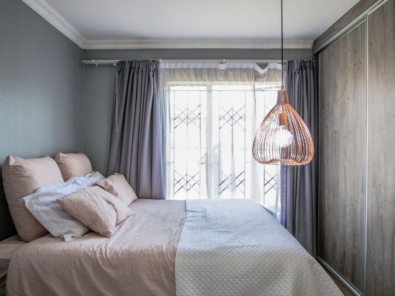 A well-maintained bedroom featuring a built-in wardrobe, security gate on the sliding door, and modern pendant lighting.