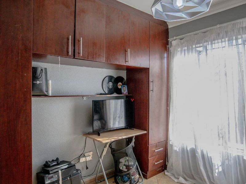 Bedroom featuring dark wood built-in cupboards, tiled flooring, and natural light through a window with sheer curtains.