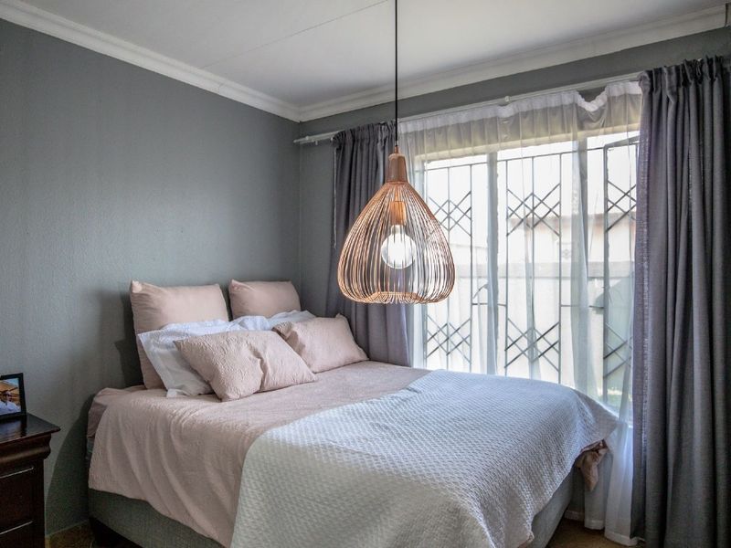 A well-maintained bedroom featuring neutral grey walls, decorative coving, and a window fitted with a security gate.