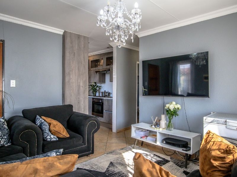 Open-plan living area featuring tiled floors, crown molding, and a seamless transition into a modern kitchen with built-in cabinetry and appliances.