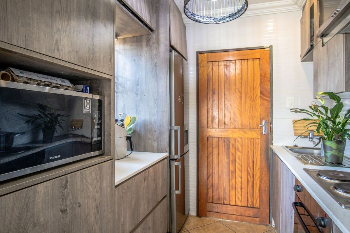 A functional kitchen featuring wood-look cabinetry, built-in microwave, integrated hob and oven, tiled backsplash, and a solid timber door.