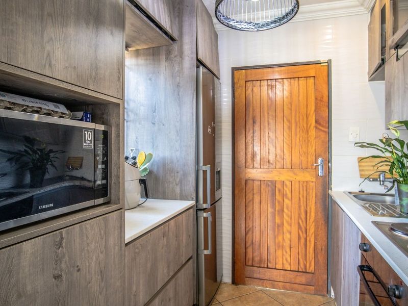 A functional kitchen featuring wood-look cabinetry, built-in microwave, integrated hob and oven, tiled backsplash, and a solid timber door.
