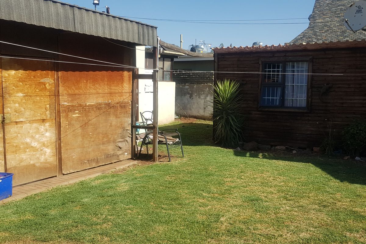 A rear garden area featuring a lawn, a timber-clad outbuilding, and a metal garage structure with a security gate.