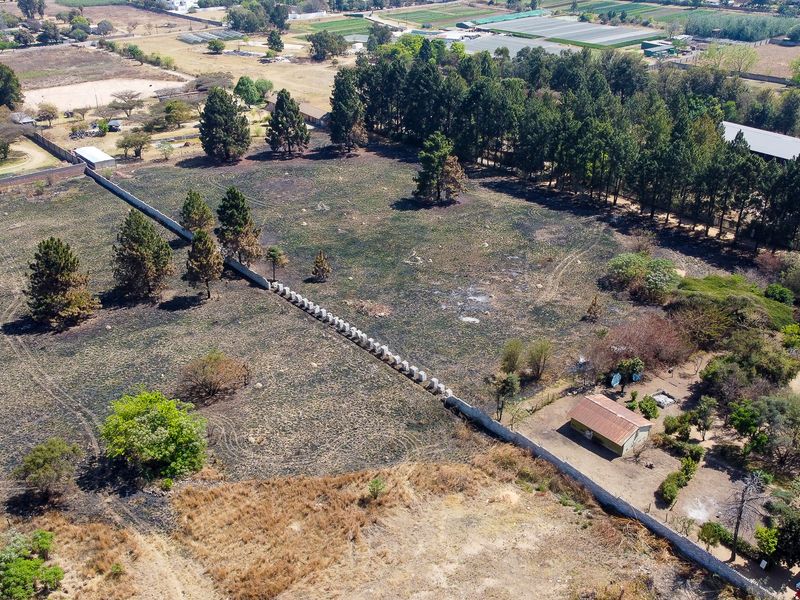 Aerial view of a large small holding property featuring extensive open land, mature trees, perimeter walling, and a small outbuilding structure.