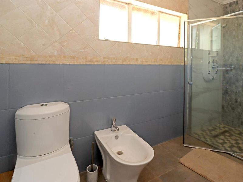 A functional bathroom featuring a toilet, bidet, and a glass-enclosed shower with tiled wall finishes.