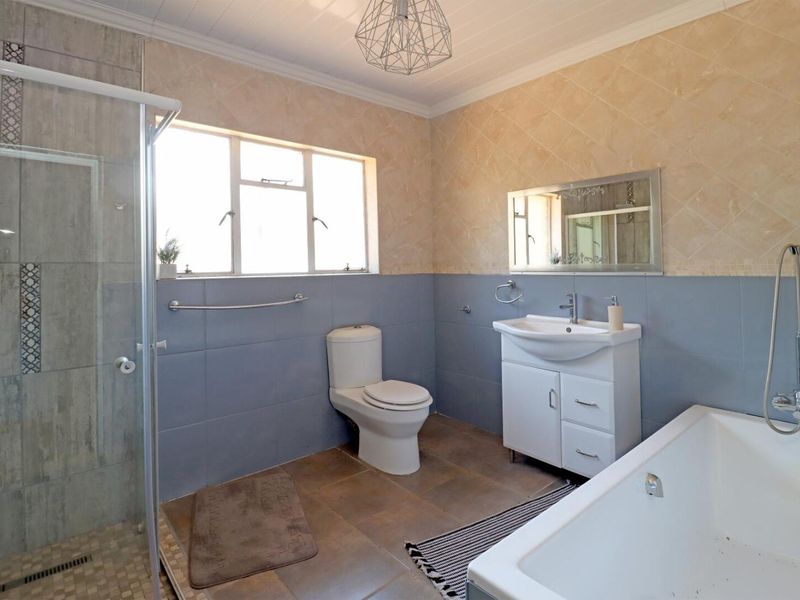 A well-maintained bathroom featuring a glass shower enclosure, a bathtub, a vanity unit with a basin, and neutral-toned wall and floor tiling.