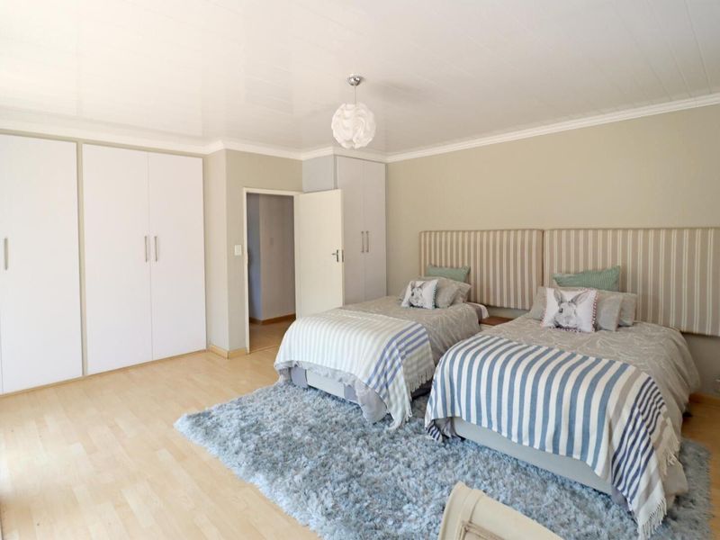 A well-maintained bedroom featuring light laminate flooring, ample built-in cupboard storage, and a clean, neutral aesthetic.