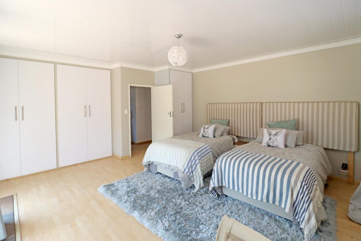 A well-maintained bedroom featuring light laminate flooring, ample built-in cupboard storage, and a clean, neutral aesthetic.