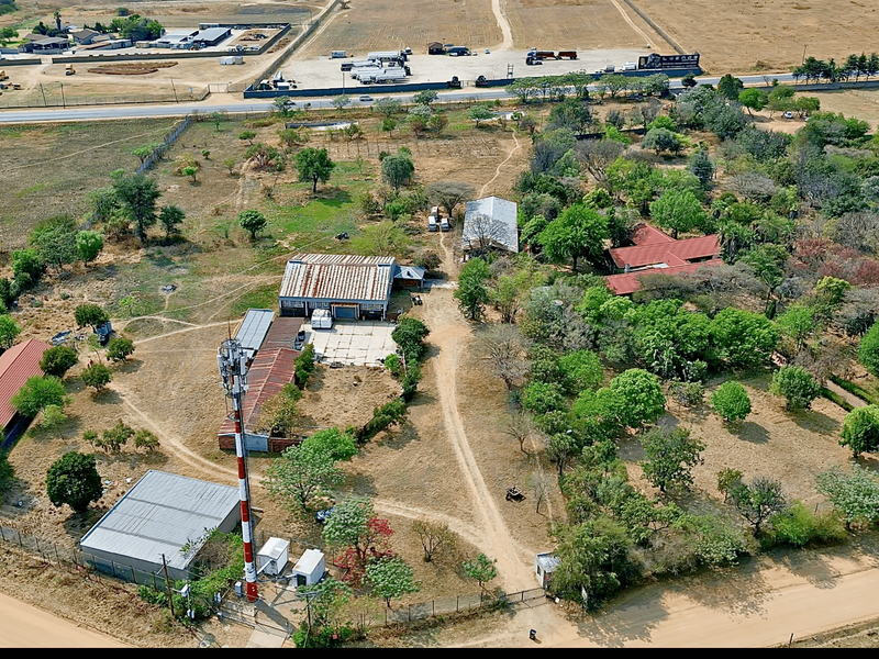 Aerial view of a large plot featuring multiple outbuildings, a telecommunications tower, mature trees, and extensive unpaved grounds.